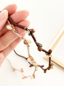 Hand holding two hairbands with branch-like design and small crystals in beige and brown color on a light background
