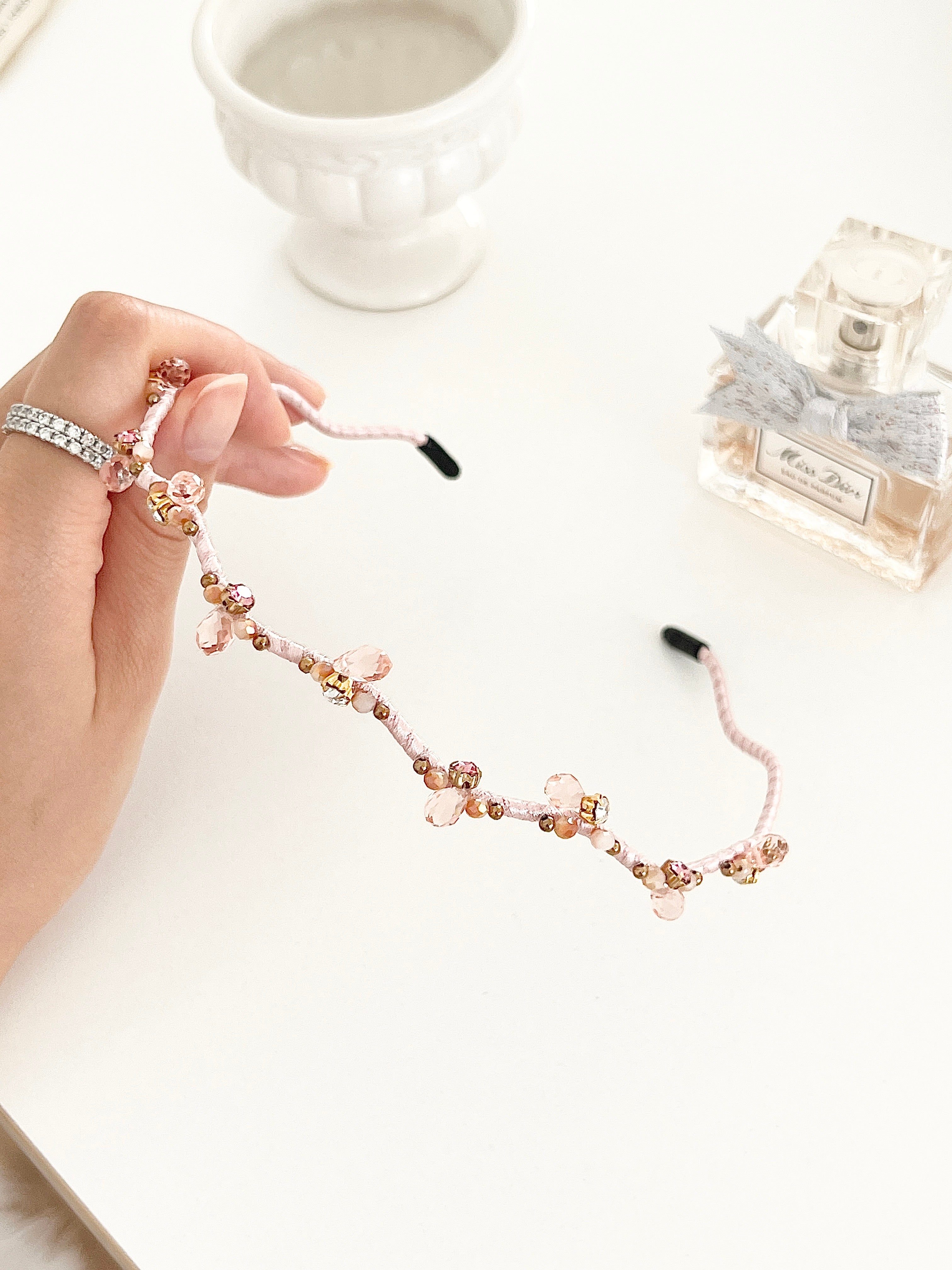 Hand holding a hairband with branch-like design and small crystal in light pink color.