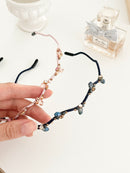 Hand holding two hairbands with branch-like design and small crystals in pink and navy color on a light background