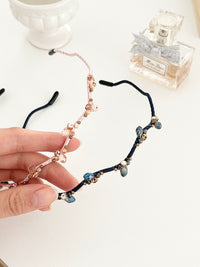 Hand holding two hairbands with branch-like design and small crystals in pink and navy color on a light background