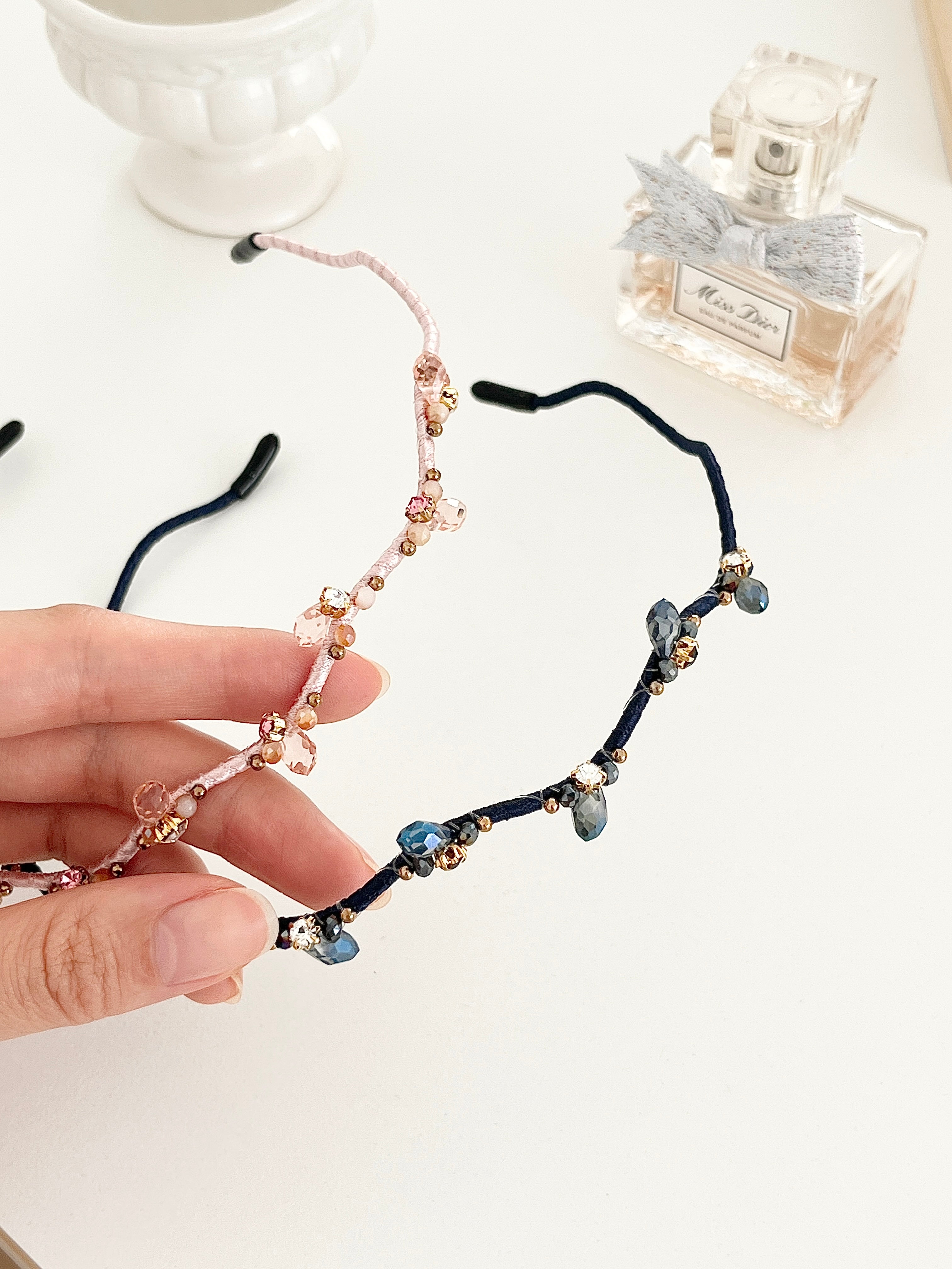 Hand holding two hairbands with branch-like design and small crystals in pink and navy color on a light background