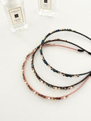 Three slim headbands with crystals, faux pearls, and beads. Includes pink-gold, brown-gold, and dark blue-black designs displayed in a white background with decorative perfume bottles. Lightweight with smooth ends for comfort.