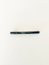 One slim rectangular hair clip in marbled shades of navy, neatly displayed on a white surface.