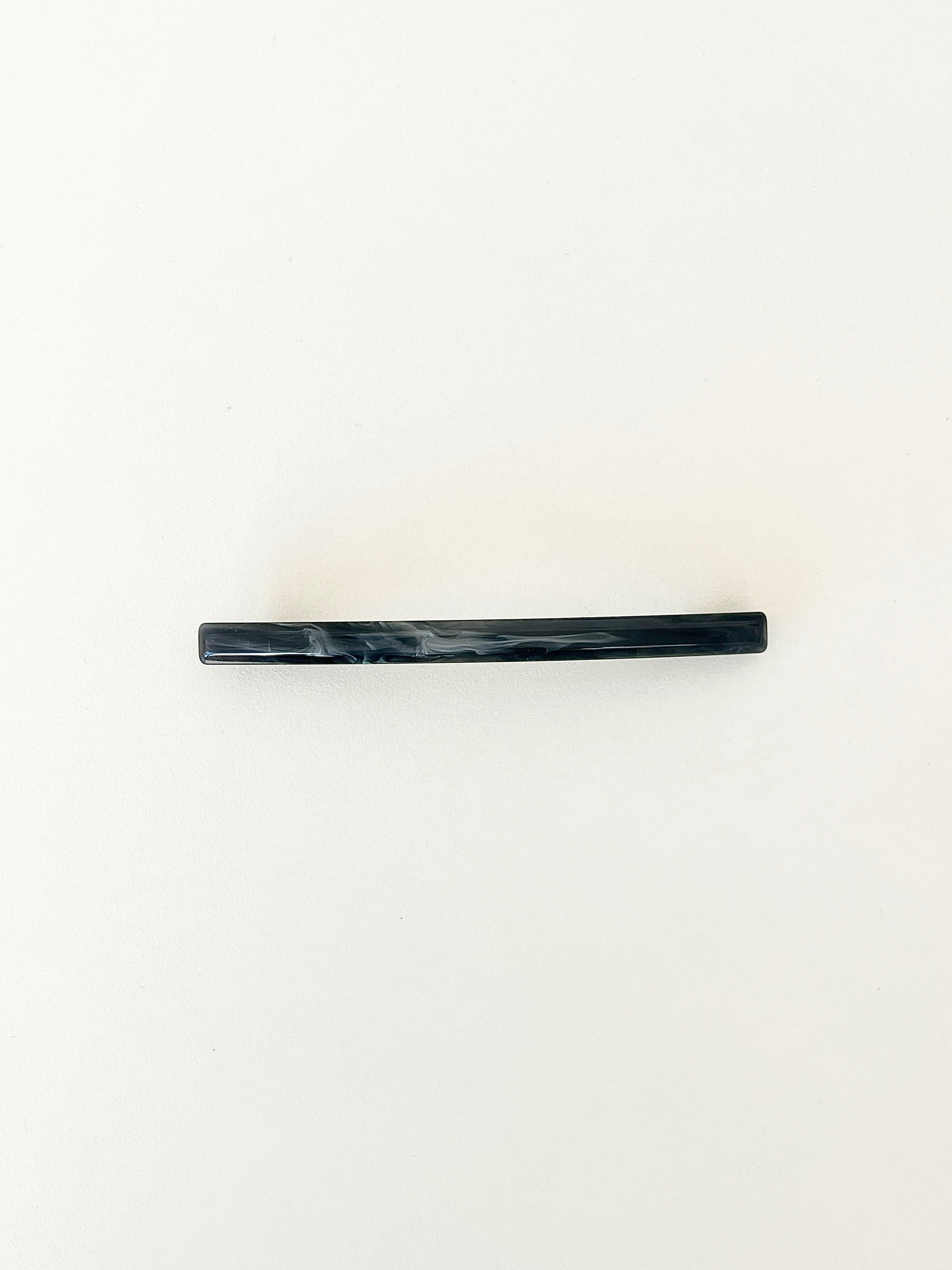 One slim rectangular hair clip in marbled shades of navy, neatly displayed on a white surface.