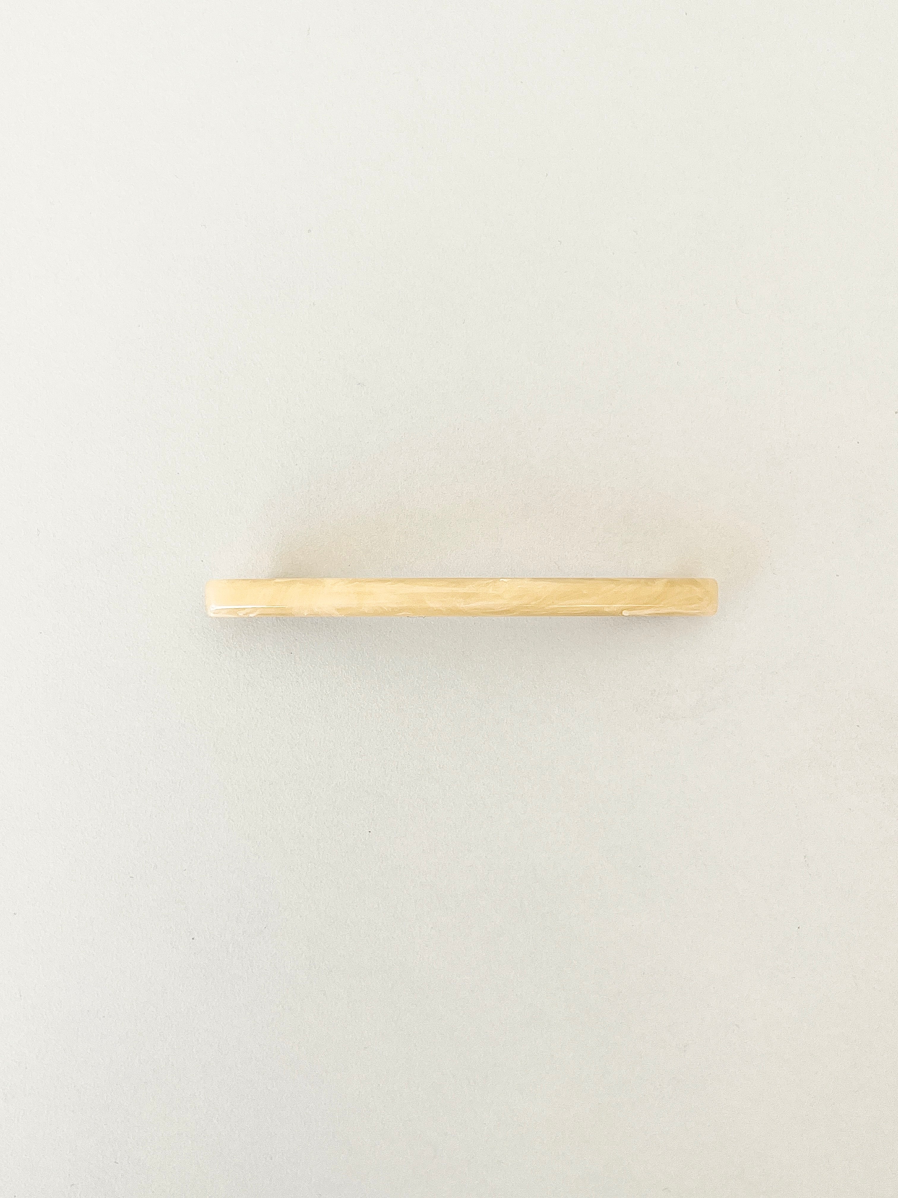 One slim rectangular hair clip in marbled shades of yellow, neatly displayed on a white surface.