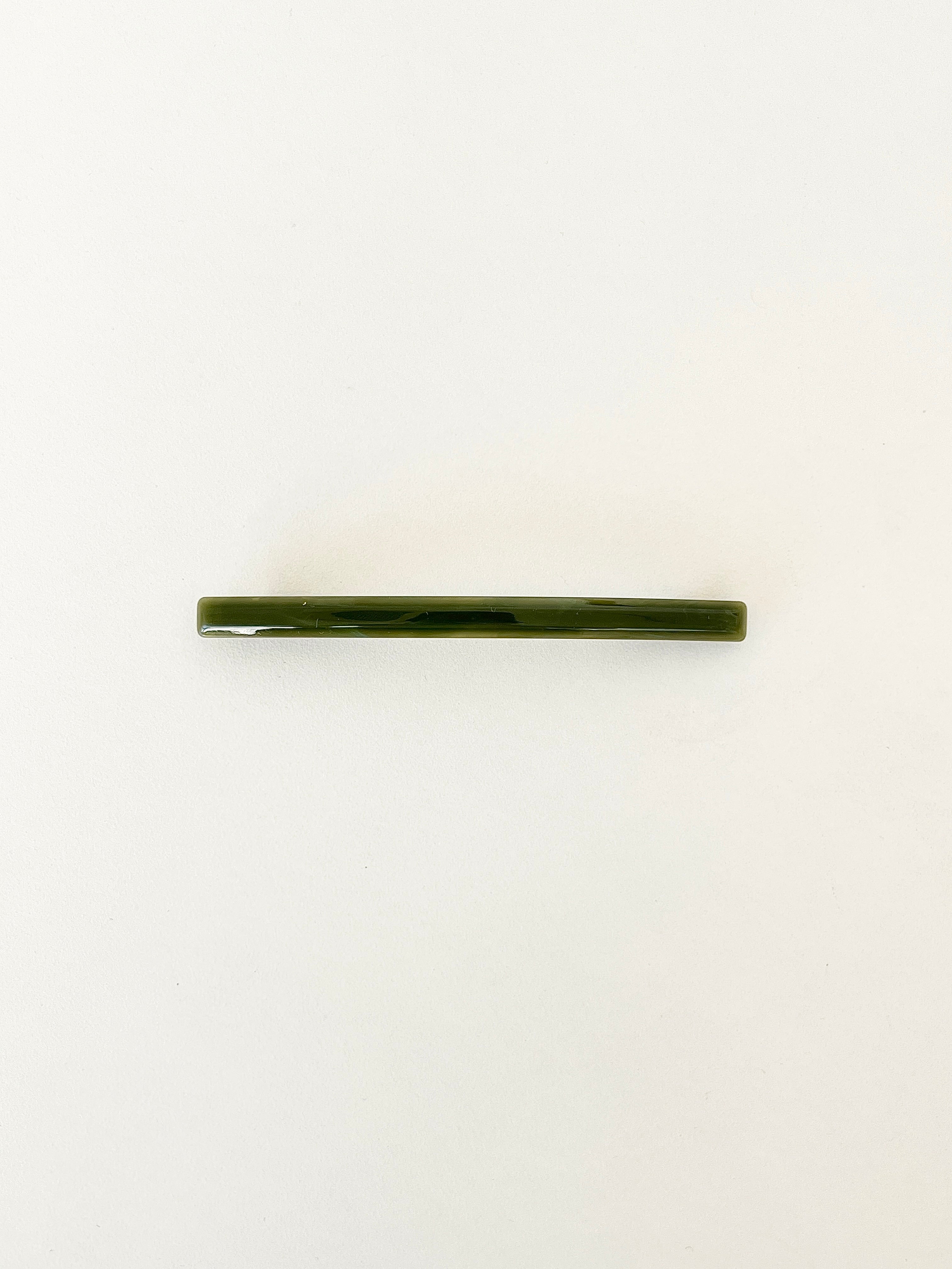 One slim rectangular hair clip in marbled shades of dark green, neatly displayed on a white surface.
