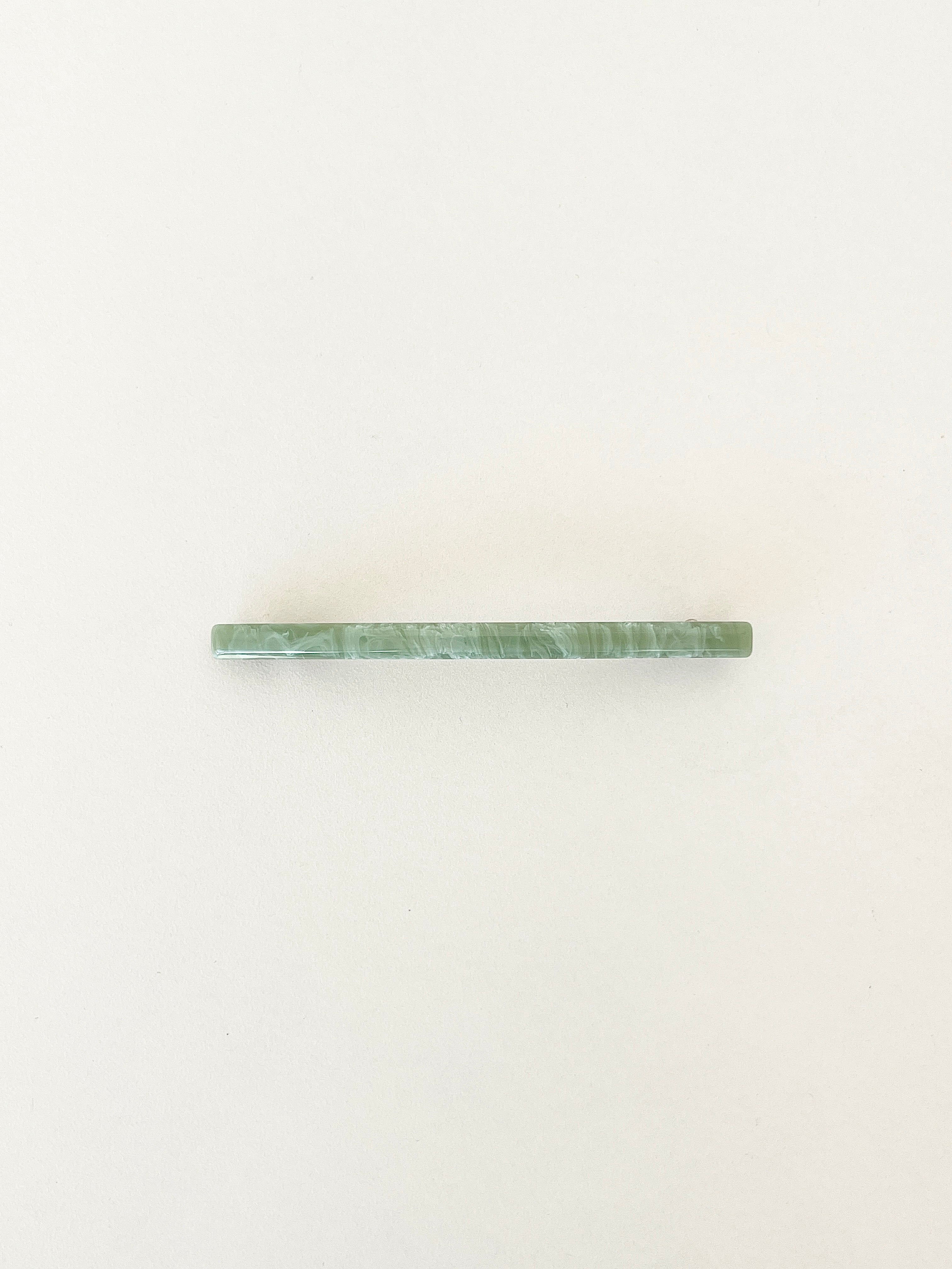 One slim rectangular hair clip in marbled shades of jade neatly displayed on a white surface.