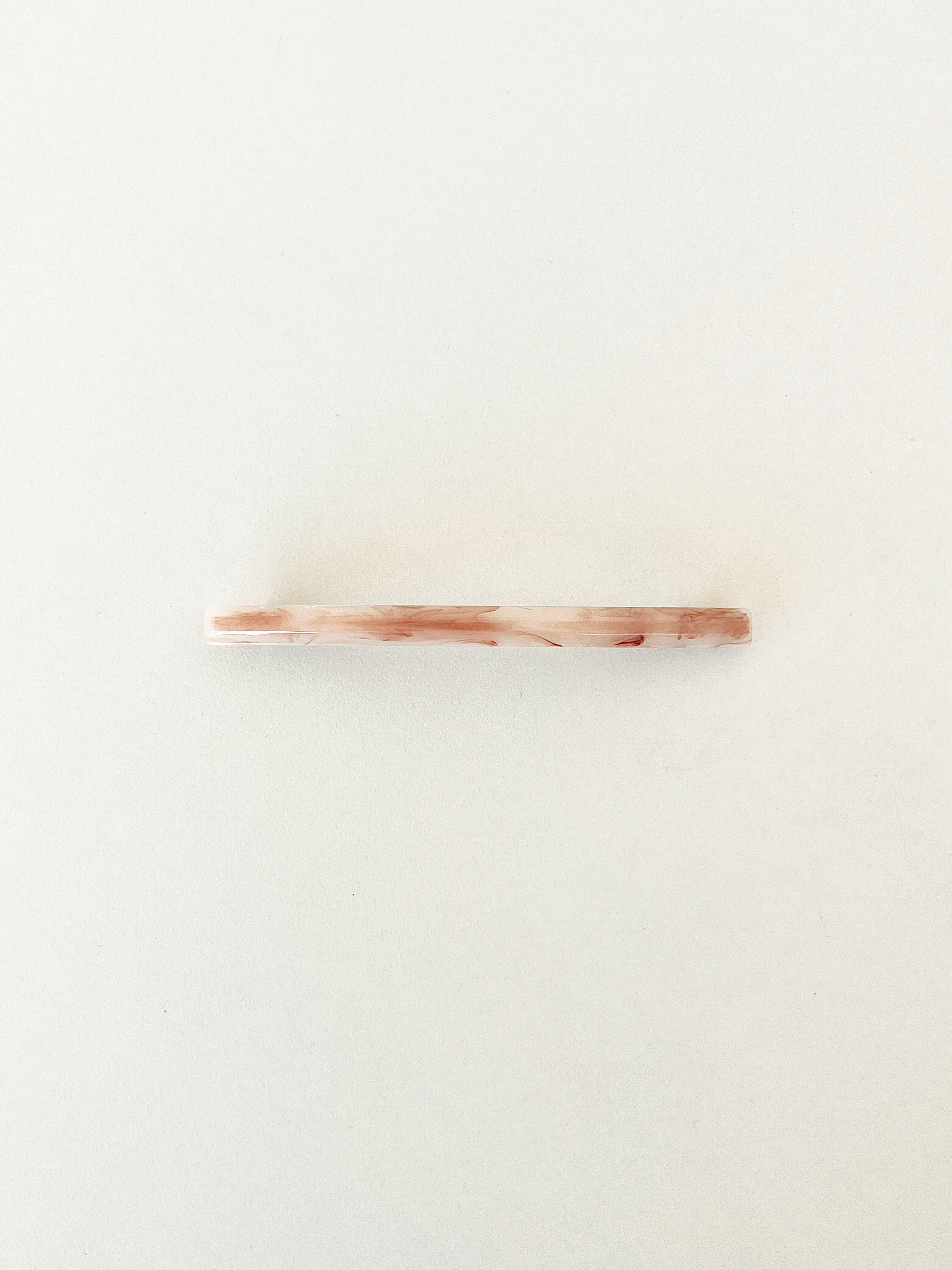 One slim rectangular hair clip in marbled shades of pink neatly displayed on a white surface.