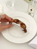 Hand holding a brown hair clip on a white plate with a bottle of Jo Malone perfume in the background.
