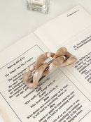 Beige hair clip in chain-link design on a book with a perfume bottle in the background.