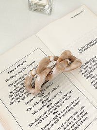 Beige hair clip in chain-link design on a book with a perfume bottle in the background.