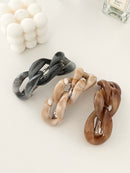 Three chain-link designed hair clips displayed with candle and perfume bottle in white background.