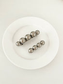 One matching sets of pearl-like ball hair clips, each set including one large and one small clip, in metallic gray, displayed on a white plate with white surface.