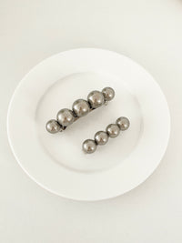 One matching sets of pearl-like ball hair clips, each set including one large and one small clip, in metallic gray, displayed on a white plate with white surface.
