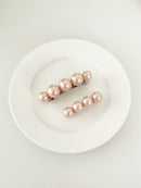 One matching sets of pearl-like ball hair clips, each set including one large and one small clip, blush pink, displayed on a white plate with white surface.