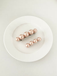 One matching sets of pearl-like ball hair clips, each set including one large and one small clip, blush pink, displayed on a white plate with white surface.