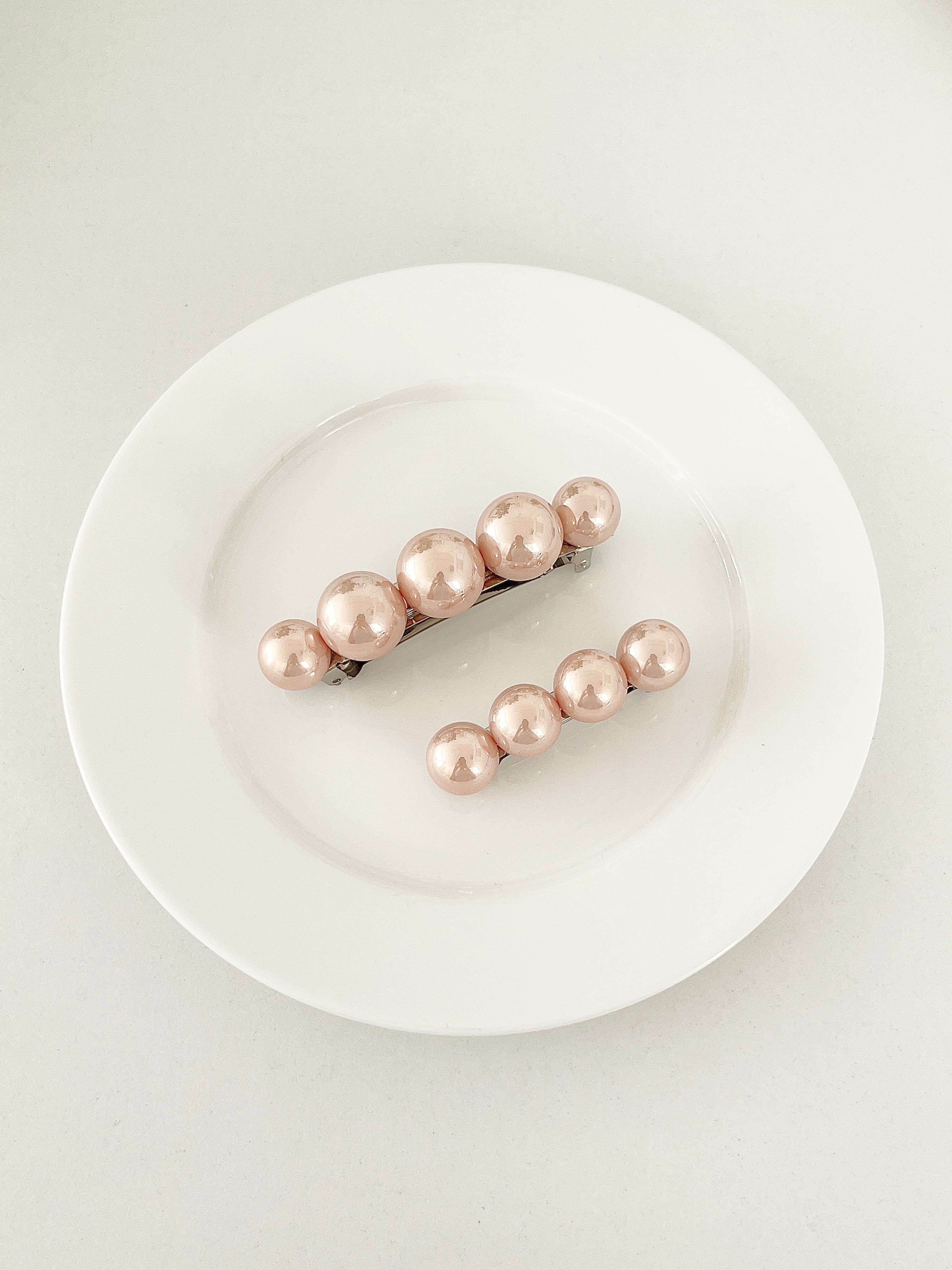 One matching sets of pearl-like ball hair clips, each set including one large and one small clip, blush pink, displayed on a white plate with white surface.