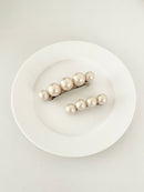 One matching sets of pearl-like ball hair clips, each set including one large and one small clip, in ivory tones, displayed on a white plate with white surface.