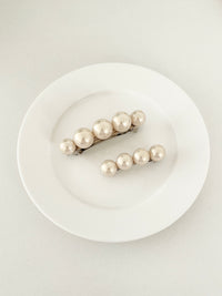 One matching sets of pearl-like ball hair clips, each set including one large and one small clip, in ivory tones, displayed on a white plate with white surface.
