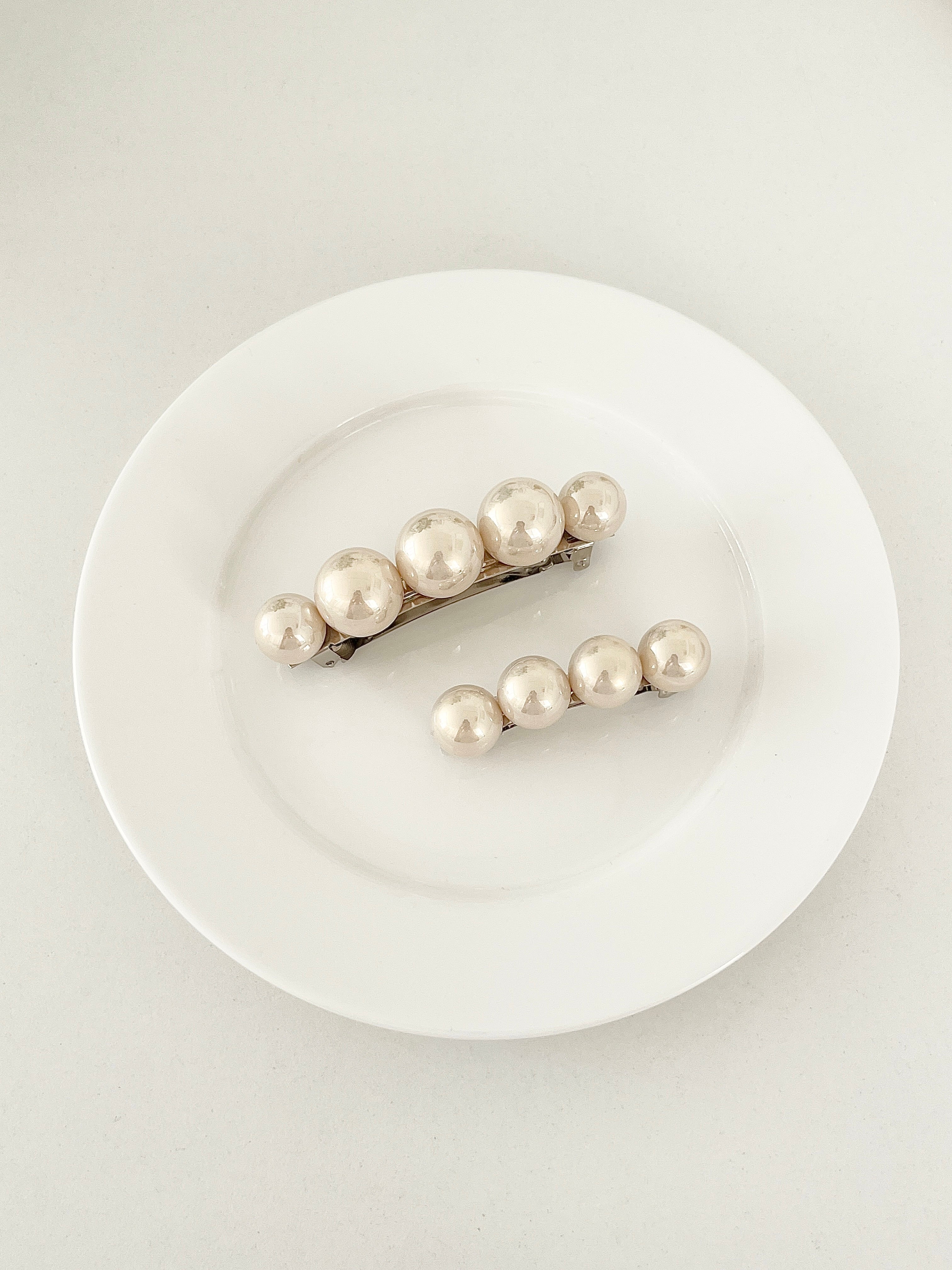 One matching sets of pearl-like ball hair clips, each set including one large and one small clip, in ivory tones, displayed on a white plate with white surface.
