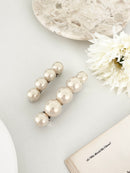 One matching sets of pearl-like ball hair clips, each set including one large and one small clip, in ivory tones, displayed on a open book with white flower on white surface.