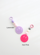 Two colorful smiley face keychains, one in lavender and one in hot pink, each featuring round pastel beads and a large smiley face charm, labeled with their color names on a white background.