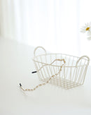 A gold vine-style headband with alternating white pearls and crystals, displayed across a white surface with a white basket and a blurred daisies in the background.