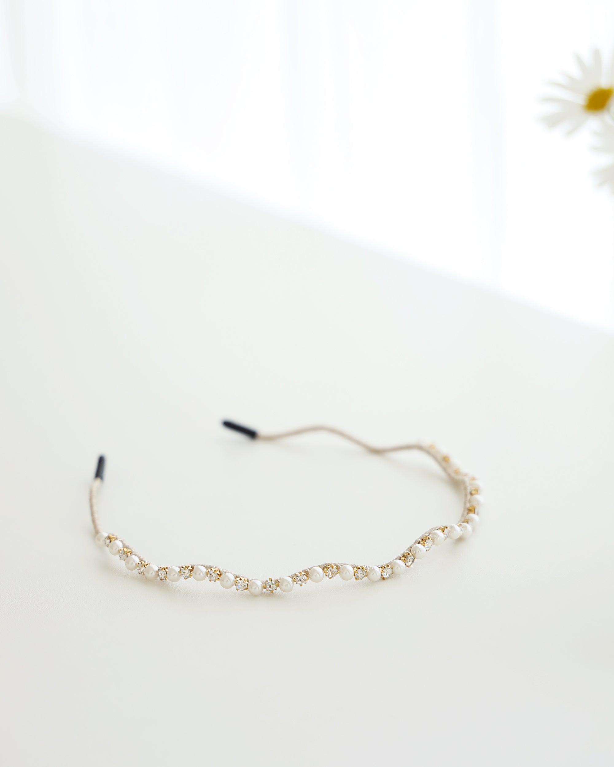 A gold vine-style headband with alternating white pearls and crystals, displayed across a white surface.