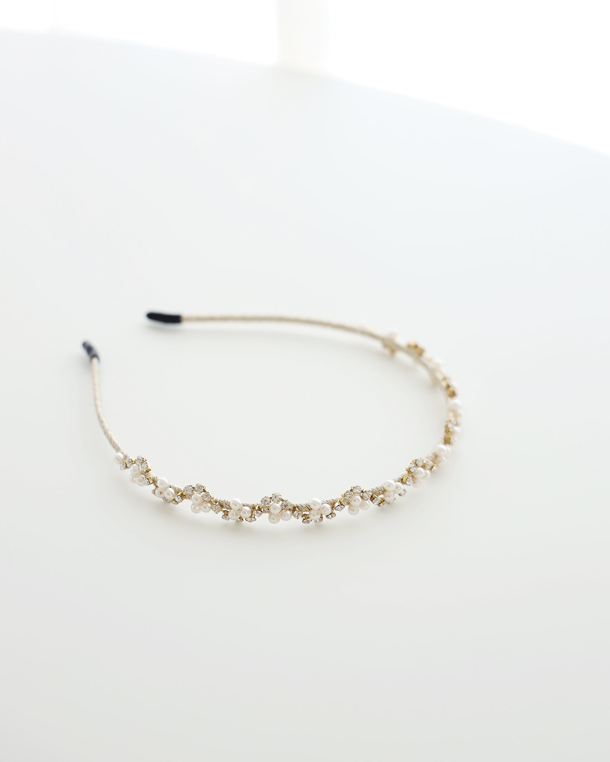 A gold floral headband adorned with small white pearls and crystals, displayed on a white surface.
