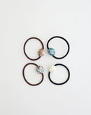 Four elastic hair ties in black and brown, each featuring a glossy mosaic-style bead in ivory, teal, pastel, and mauve tones, displayed on white background.