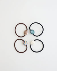 Four elastic hair ties in black and brown, each featuring a glossy mosaic-style bead in ivory, teal, pastel, and mauve tones, displayed on white background.