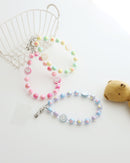 Three pastel beaded phone straps with glossy round beads and one smiley face bead. Available in pink, blue, or yellow color themes. Comes with a clear plastic phone tab that fits between the phone and case, with a metal clasp to attach the strap displayed on white background