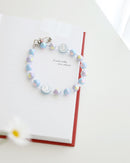 Pastel blue and lavender beaded phone strap with glossy round beads and one white smiley face bead with blue smile. Comes with a clear plastic phone tab and metal clasp for attachment displayed on a book