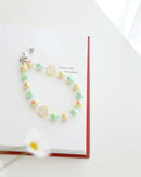 Pastel blue and lavender beaded phone strap with glossy round beads and one white smiley face bead with blue smile. Comes with a clear plastic phone tab and metal clasp for attachment displayed on a book