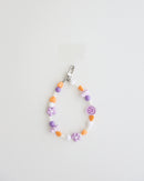 A pastel beaded cell phone strap featuring purple, orange, and white beads with flower and heart accents, plus a small smiley charm. It includes a clear holder insert that slips into a phone case for secure attachment.