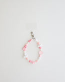 A pastel beaded cell phone strap featuring pink, soft pink, and white beads with flower and heart accents, plus a small smiley charm. It includes a clear holder insert that slips into a phone case for secure attachment.