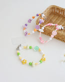 Three colorful cell phone straps made with pastel beads, hearts, flowers, and smiley charms. Each strap has a clear holder designed to slip into a phone case for easy attachment, displayed on a white background with basket.